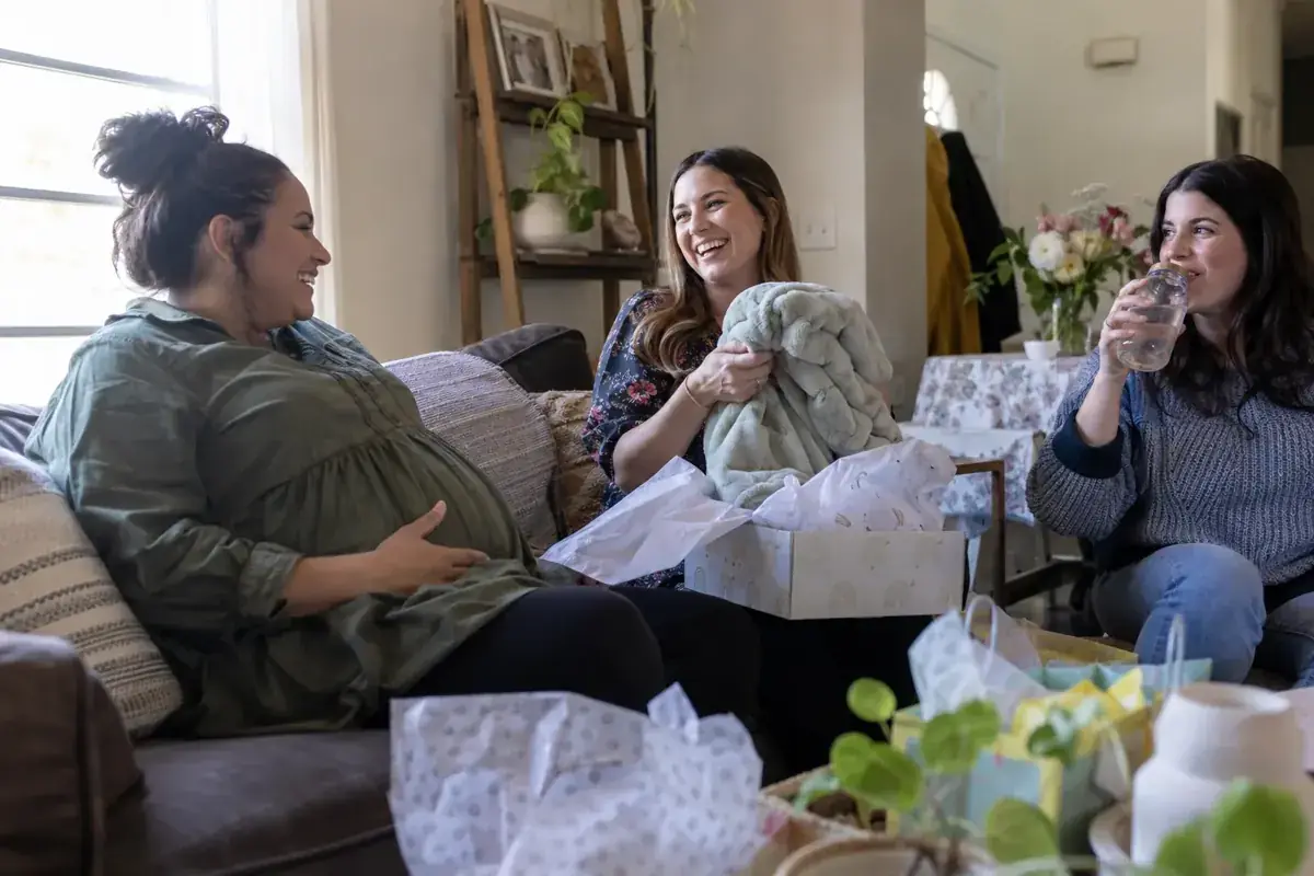 Tres amigas conversan durante un baby shower en una sala familiar.