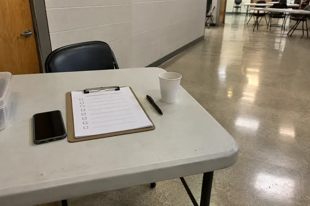 Lista, teléfono, bolígrafo y vaso sobre una mesa sencilla de recepción.