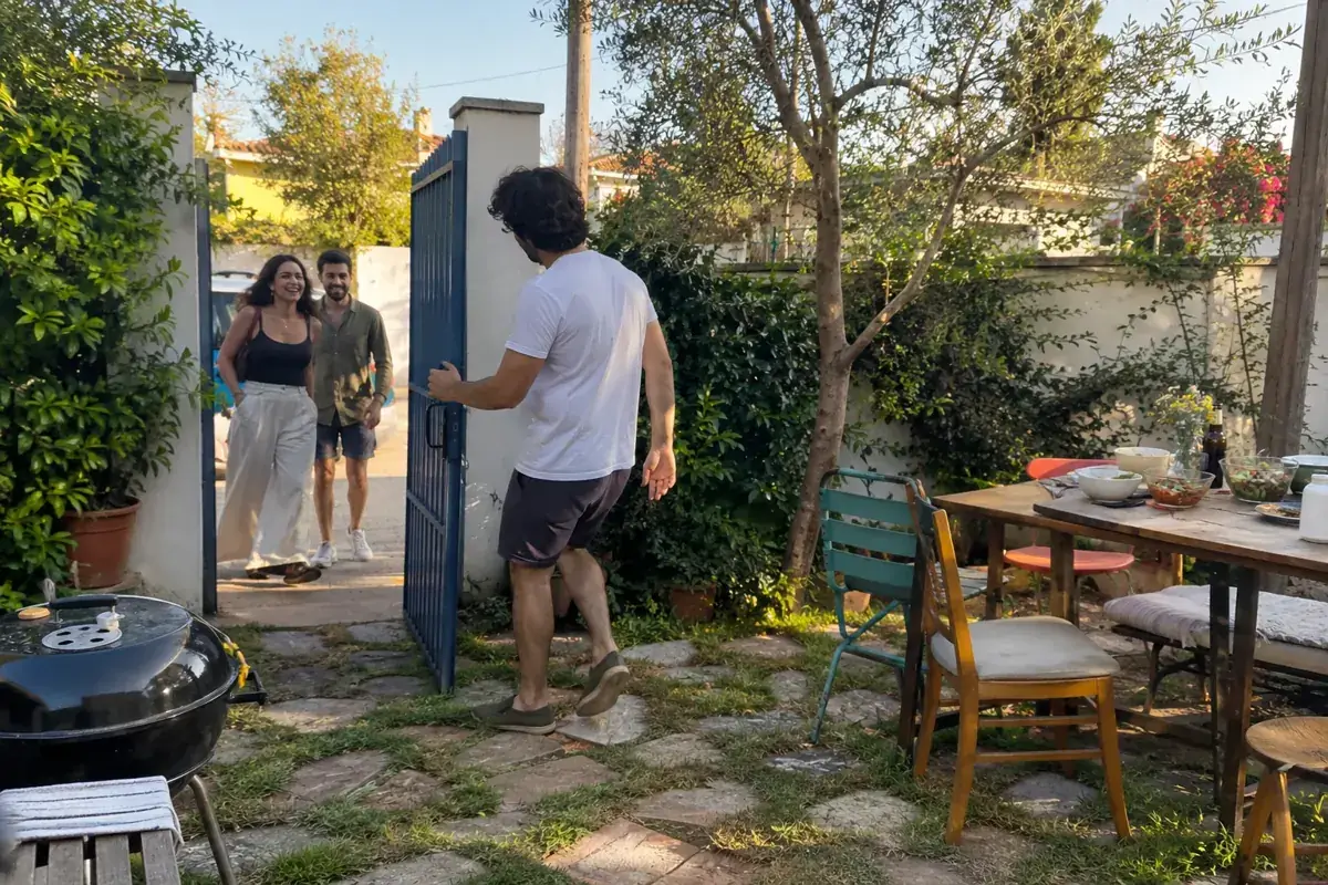 Un anfitrión abre la entrada de un patio a dos personas que llegan a la reunión.