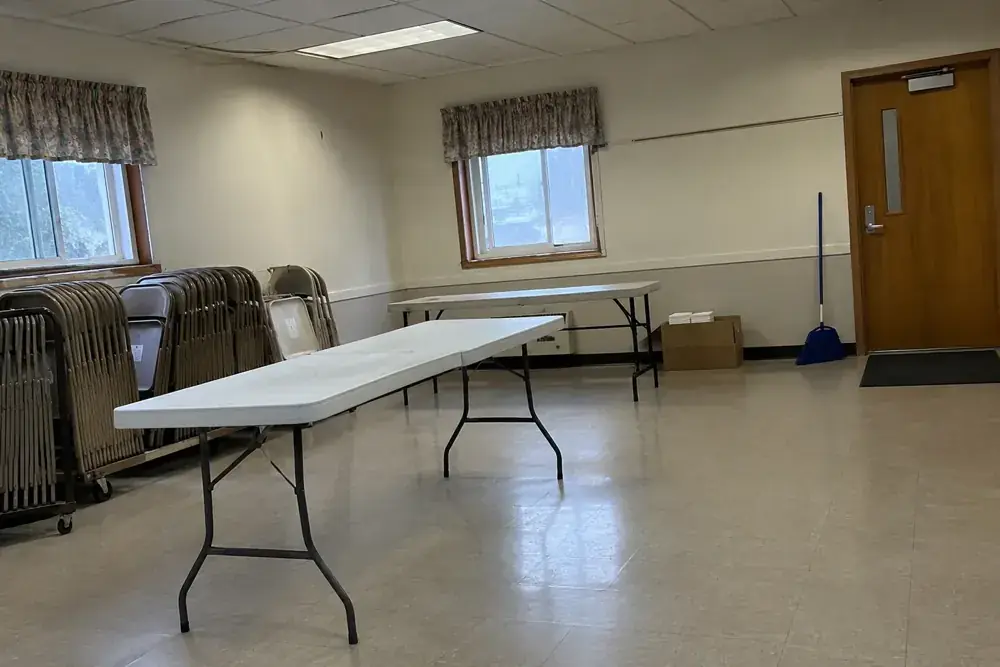 Salón comunitario con mesas en montaje, sillas plegadas y materiales de preparación.
