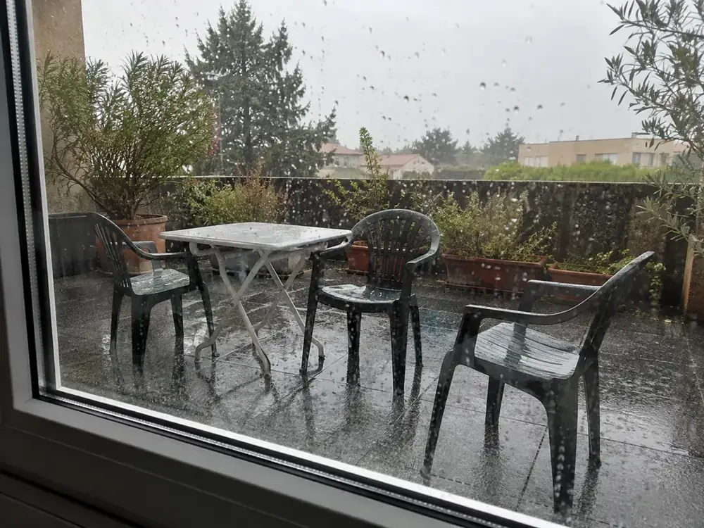 Imagen generada: Patio mojado visto desde el interior a través de una ventana con lluvia.