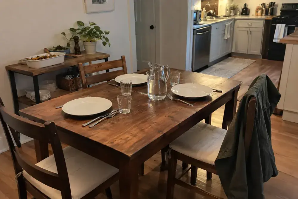Mesa doméstica preparada con platos, agua y espacio entre las sillas.