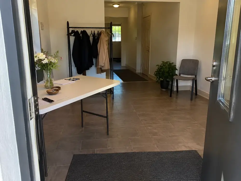 Imagen generada: Entrada despejada de una sala con mesa, sillas y perchero.