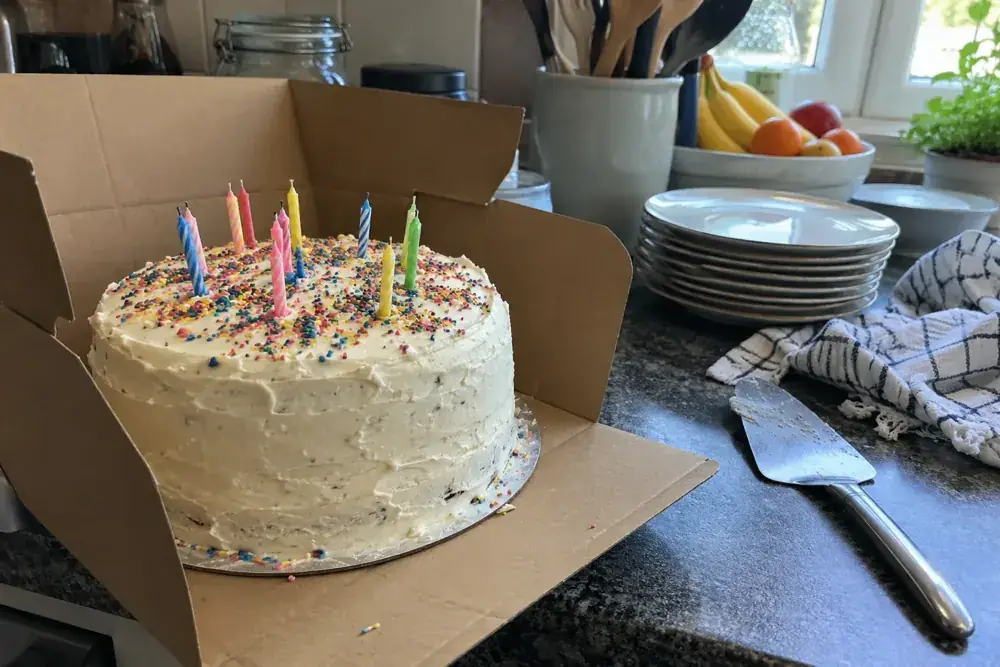 Pastel con velas sin encender, platos y pala para servir sobre una encimera.