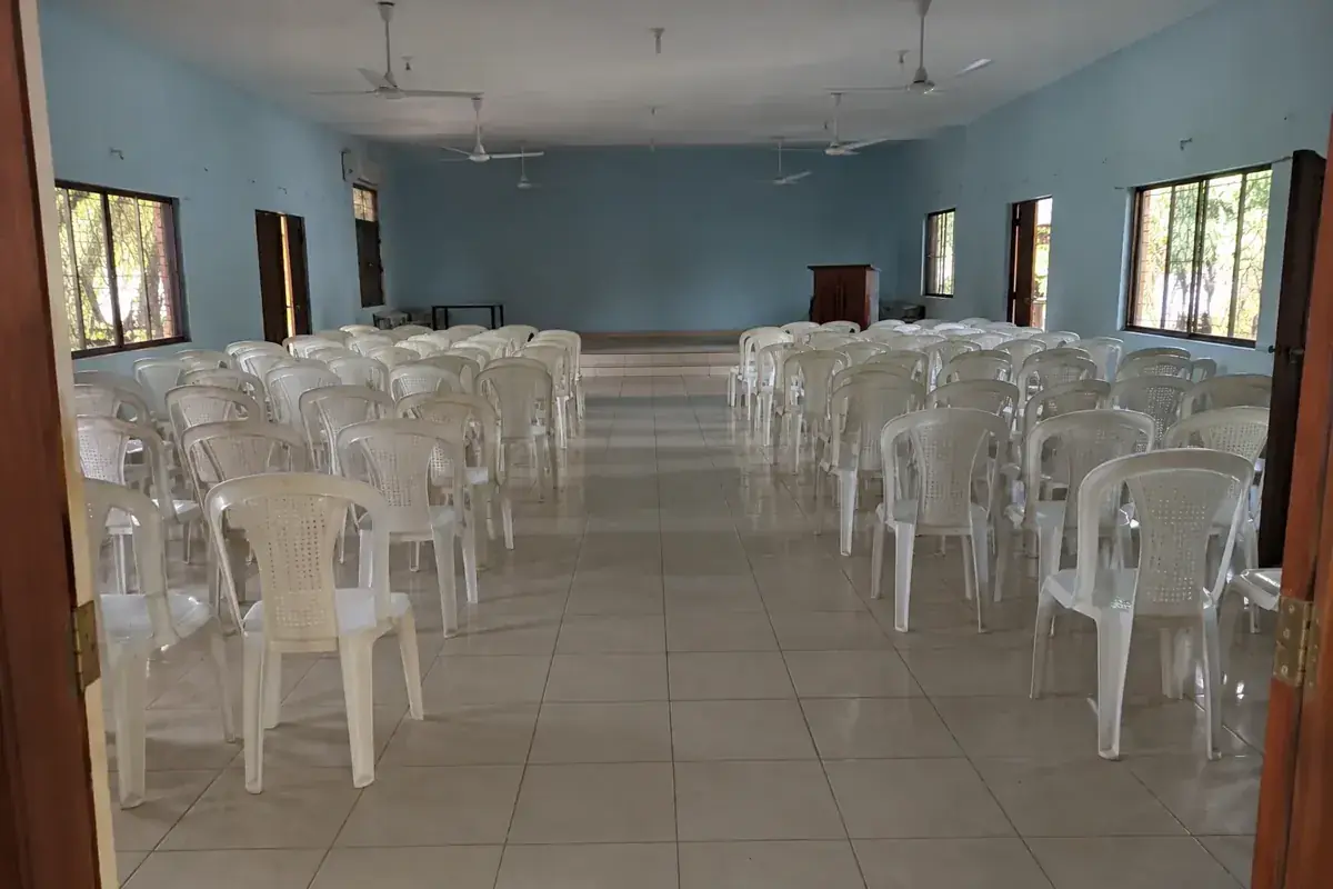 Salón comunitario vacío con filas de sillas y un pasillo despejado.