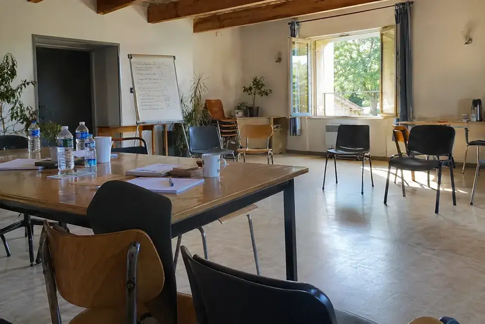 Imagen generada: Sala comunitaria con sillas distintas, mesas y botellas de agua antes de la reunión.