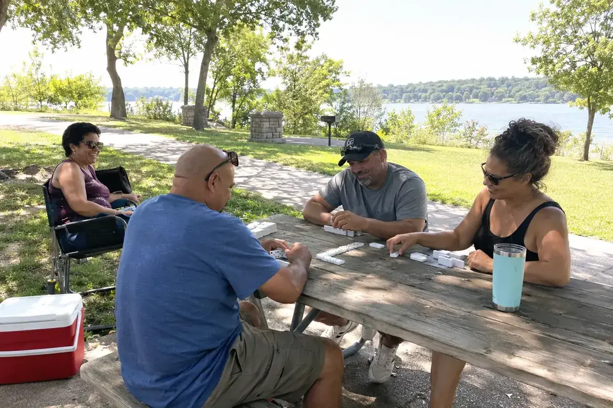 Un grupo juega dominó junto a una mesa de picnic en un parque.