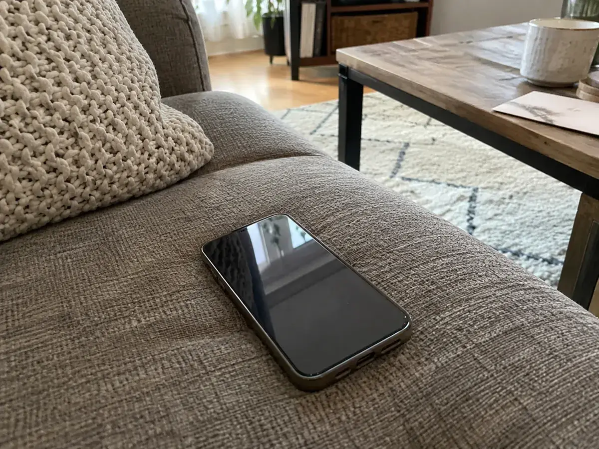 Imagen generada: Teléfono con la pantalla apagada sobre el asiento de un sofá.