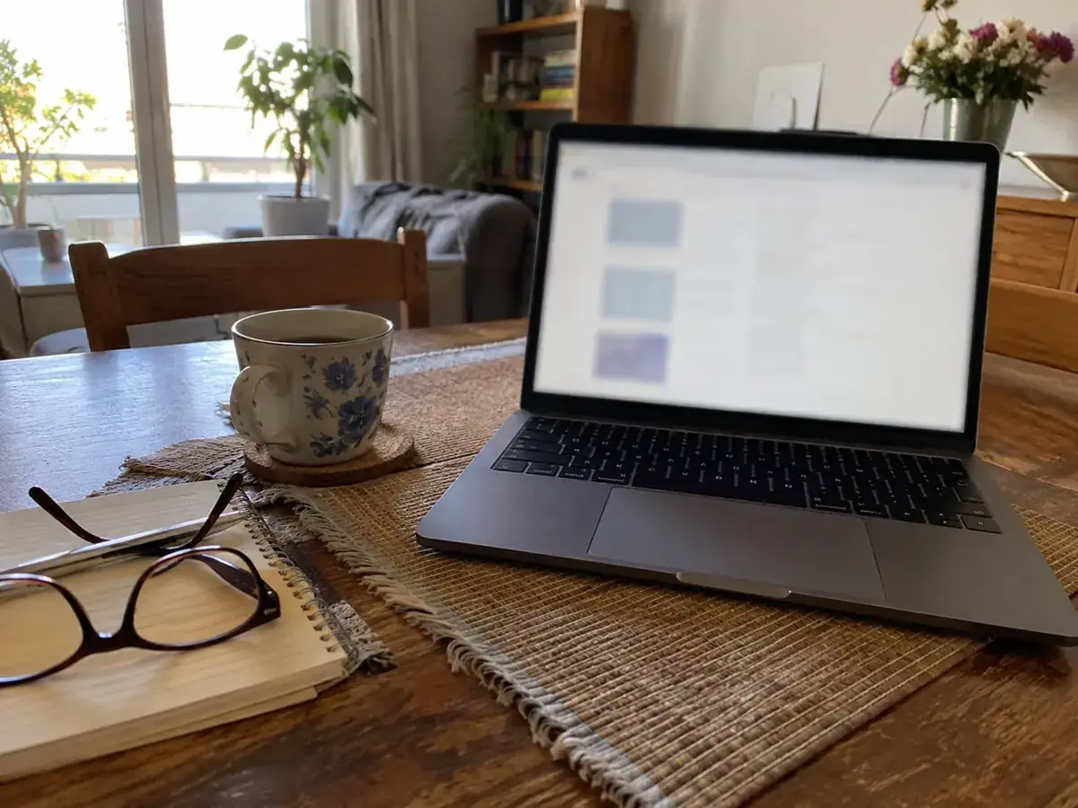 Imagen generada: Computadora portátil abierta sobre una mesa de comedor junto a una taza.
