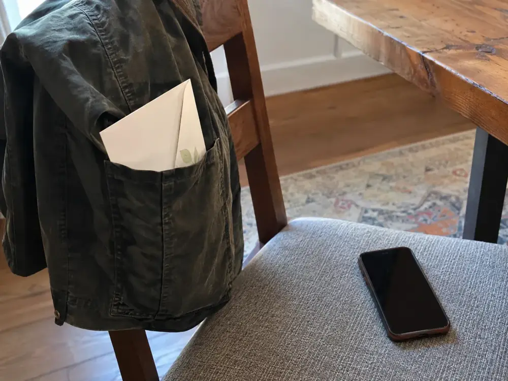 Imagen generada: Sobre de papel en el bolsillo de una chaqueta y teléfono sobre una silla.