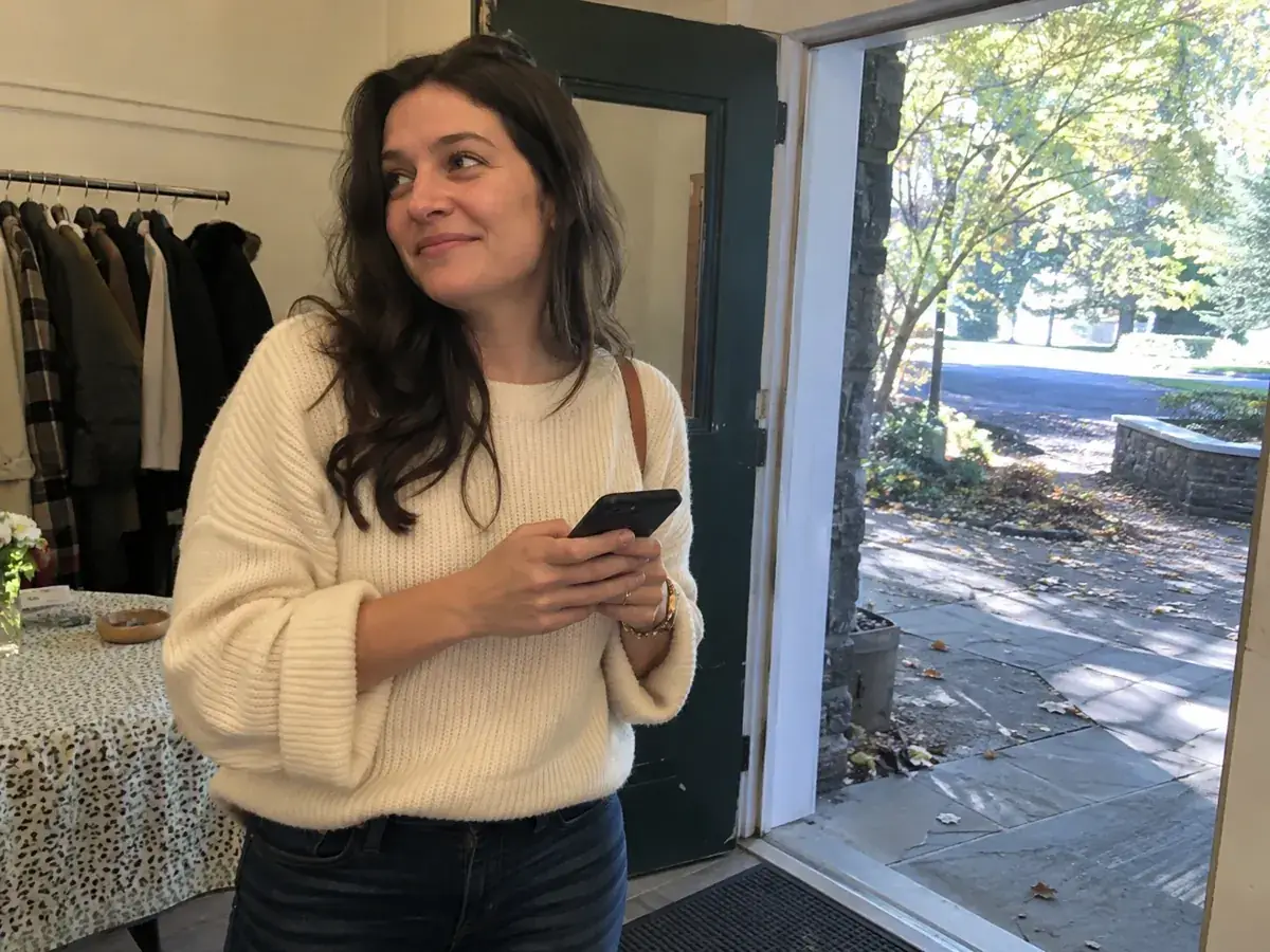 Imagen generada: Una mujer sostiene su teléfono junto a la entrada de una reunión.