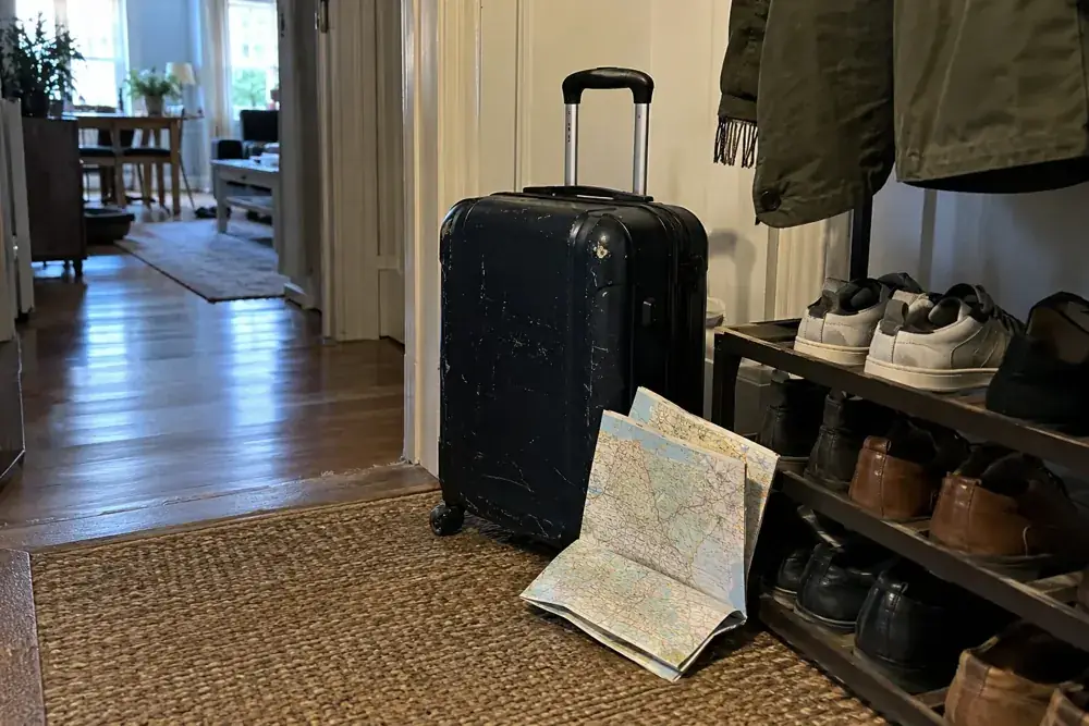 Maleta y mapa plegado junto a un zapatero en la entrada de una vivienda.