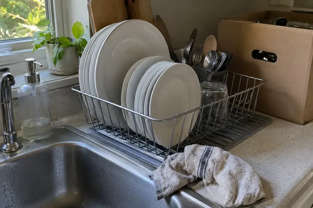 Platos limpios en un escurridor junto al fregadero y una caja para devolver utensilios.
