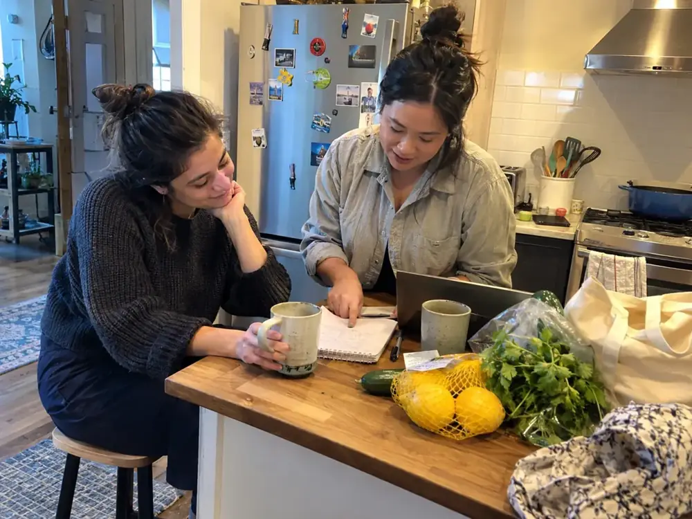 Imagen generada: Dos personas revisan juntas un cuaderno sobre la mesa de una cocina.