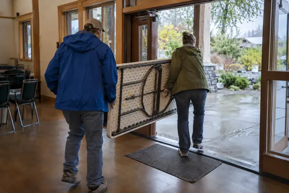 Dos personas trasladan una mesa plegable por la entrada de un salón.