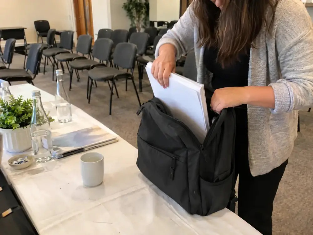Imagen generada: Una persona guarda papeles en una mochila durante la preparación de una sala.