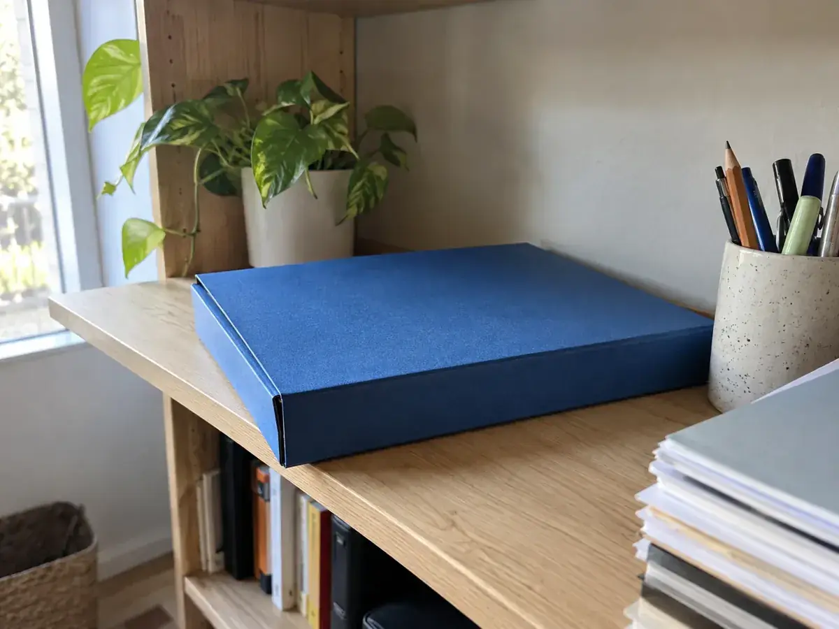 Imagen generada: Carpeta azul cerrada y bolígrafos sobre una mesa junto a una ventana.