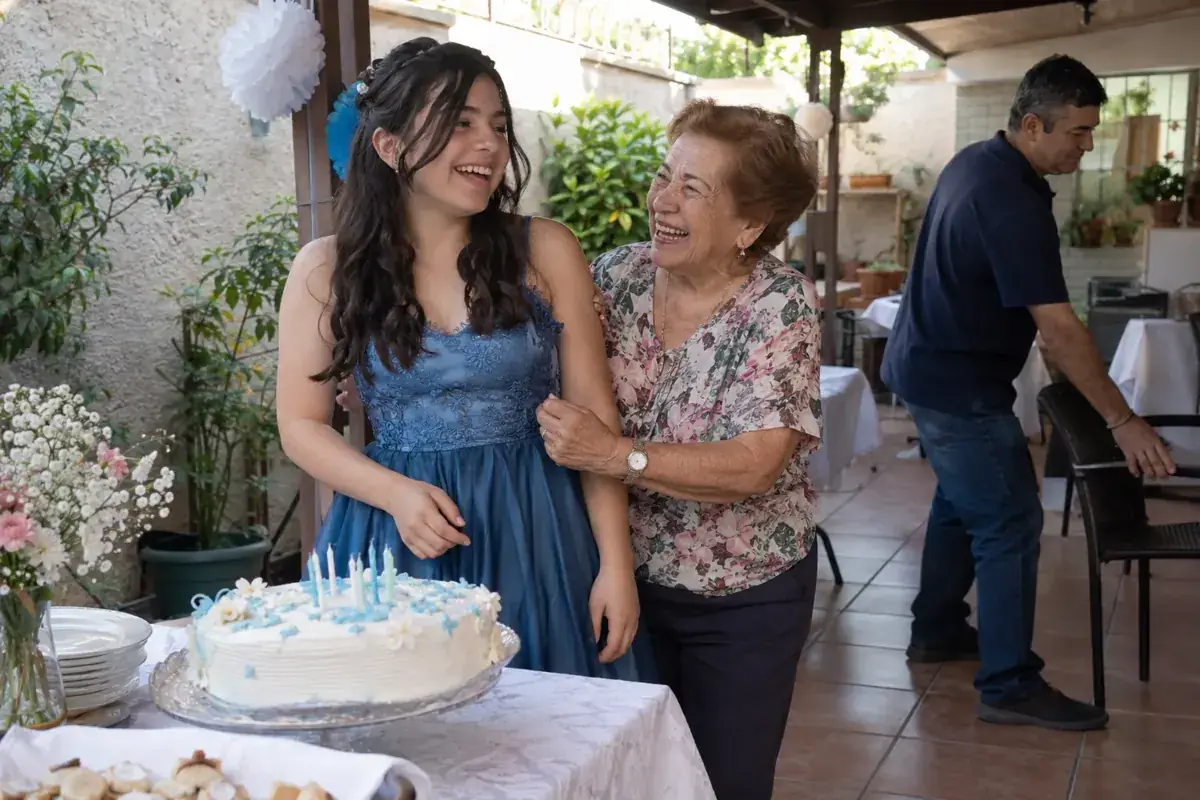 Una quinceañera y su abuela sonríen junto al pastel en un patio familiar.
