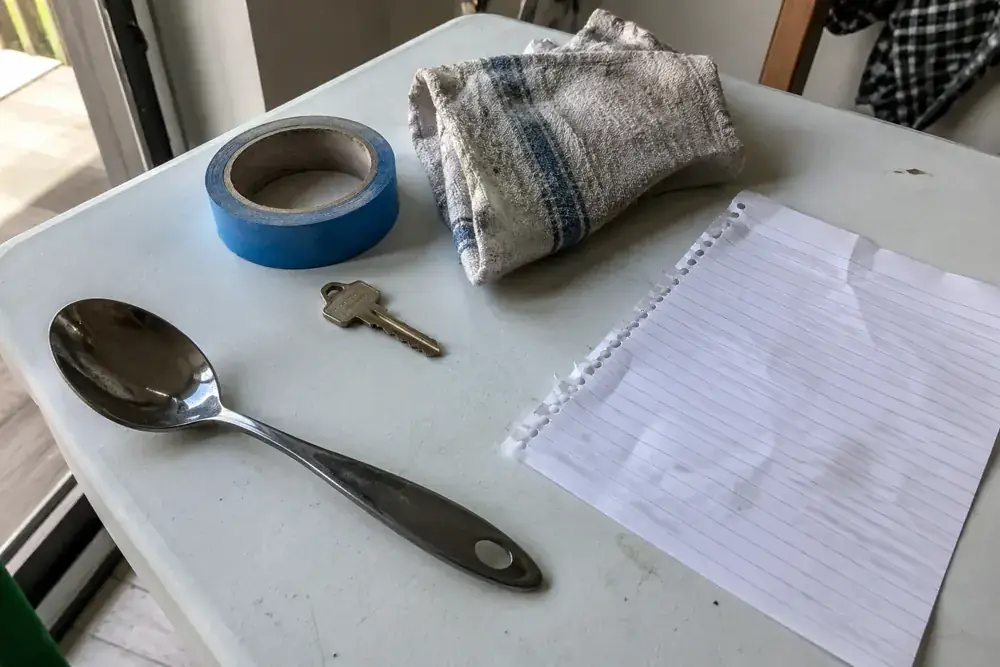 Llave, cinta, paño, cuchara y libreta sobre una mesa de trabajo.