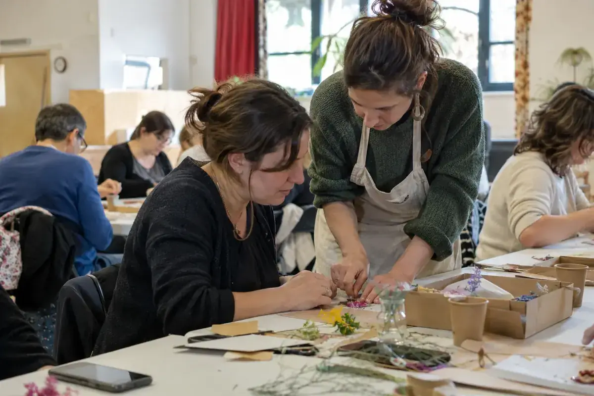 Imagen generada: Una facilitadora ayuda a una participante durante un taller creativo.